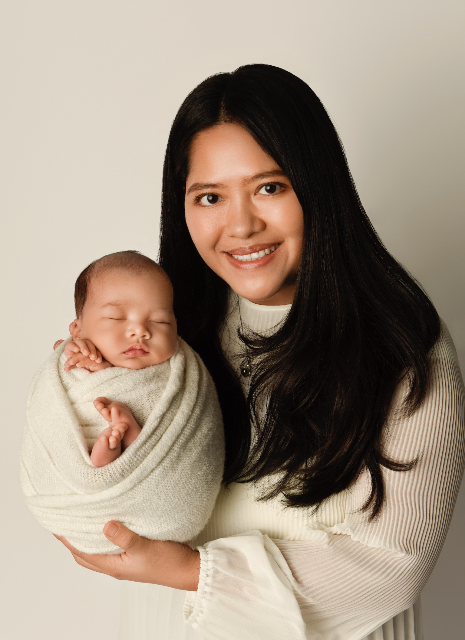 Mother in a cream outfit holding her sleeping newborn wrapped in ivory at Kayla Photography’s Ottawa studio