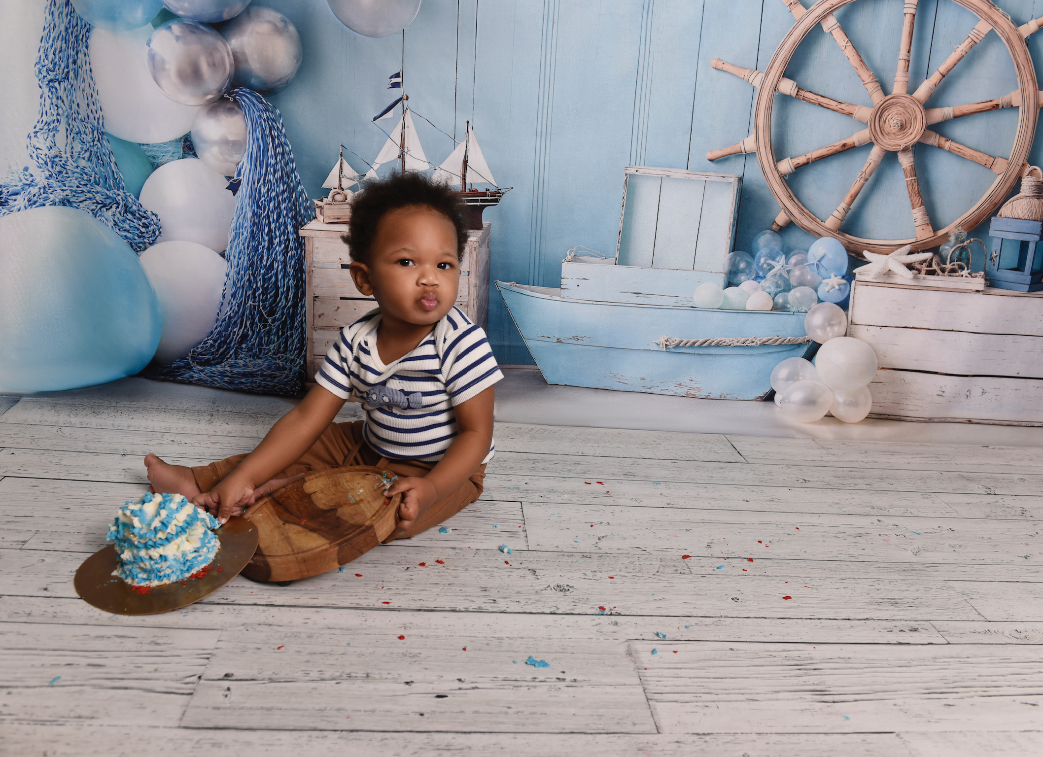 Baby in a striped outfit beside a blue birthday cake on a nautical portrait set at Kayla Photography in Ottawa