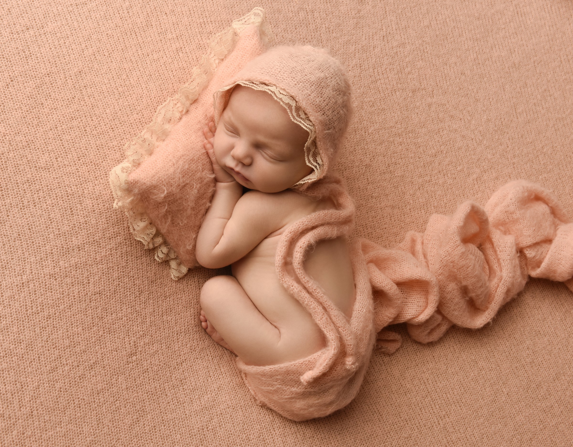 Sleeping newborn in a peach bonnet and wrap