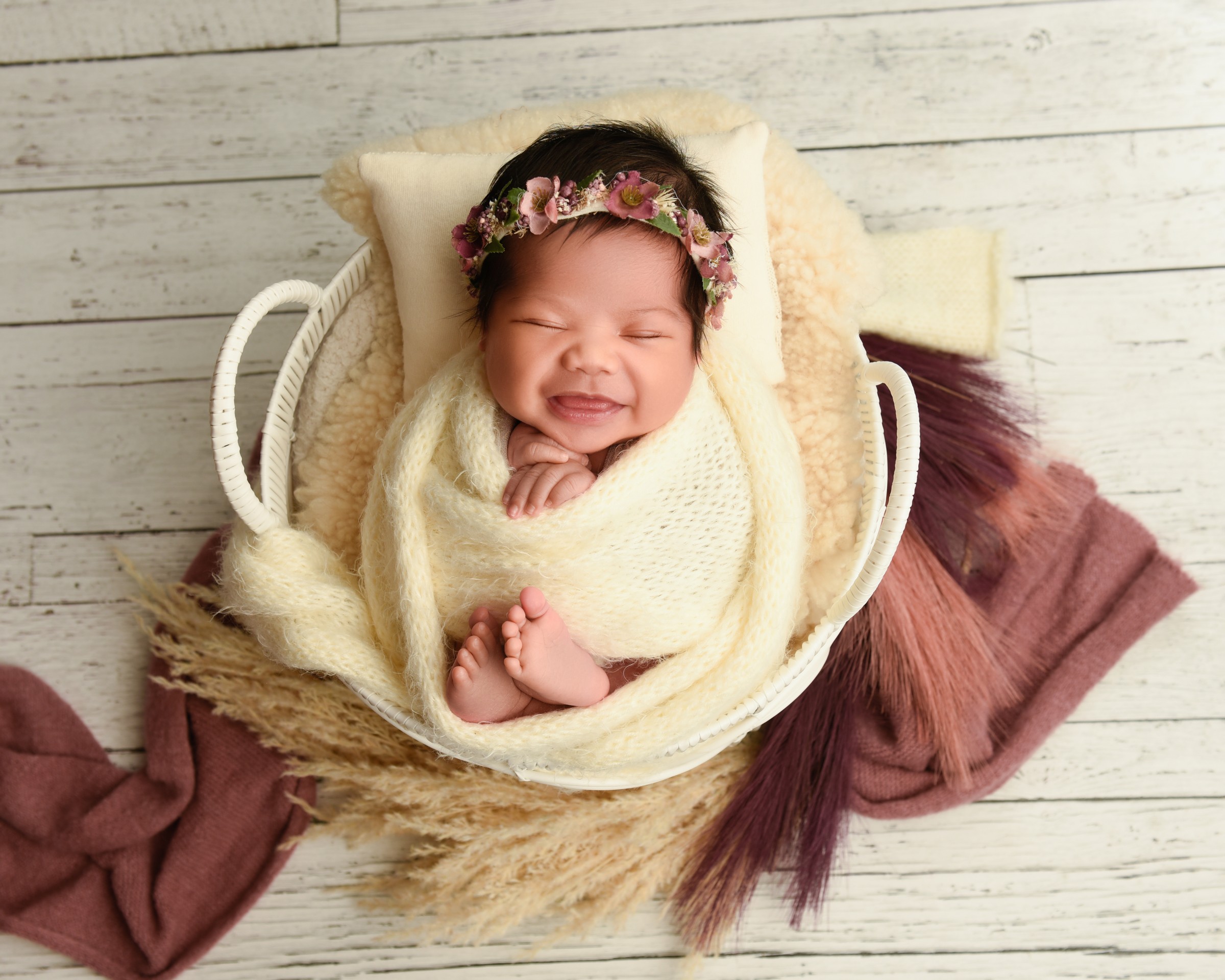 Smiling newborn in a cream wrap and floral headband