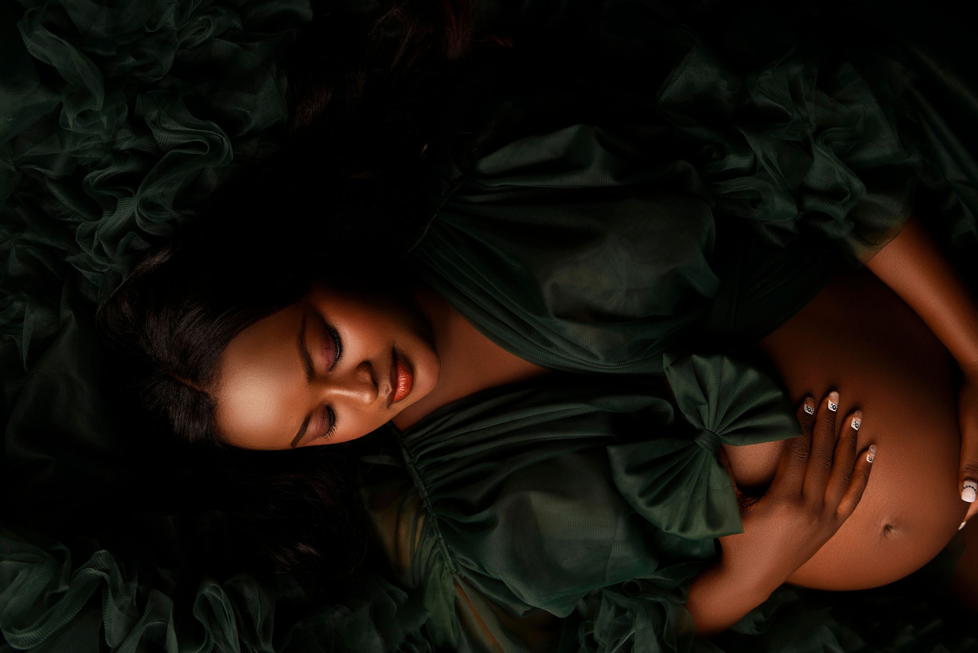 Woman lying in a flowing green maternity gown with her belly showing and her head to the left