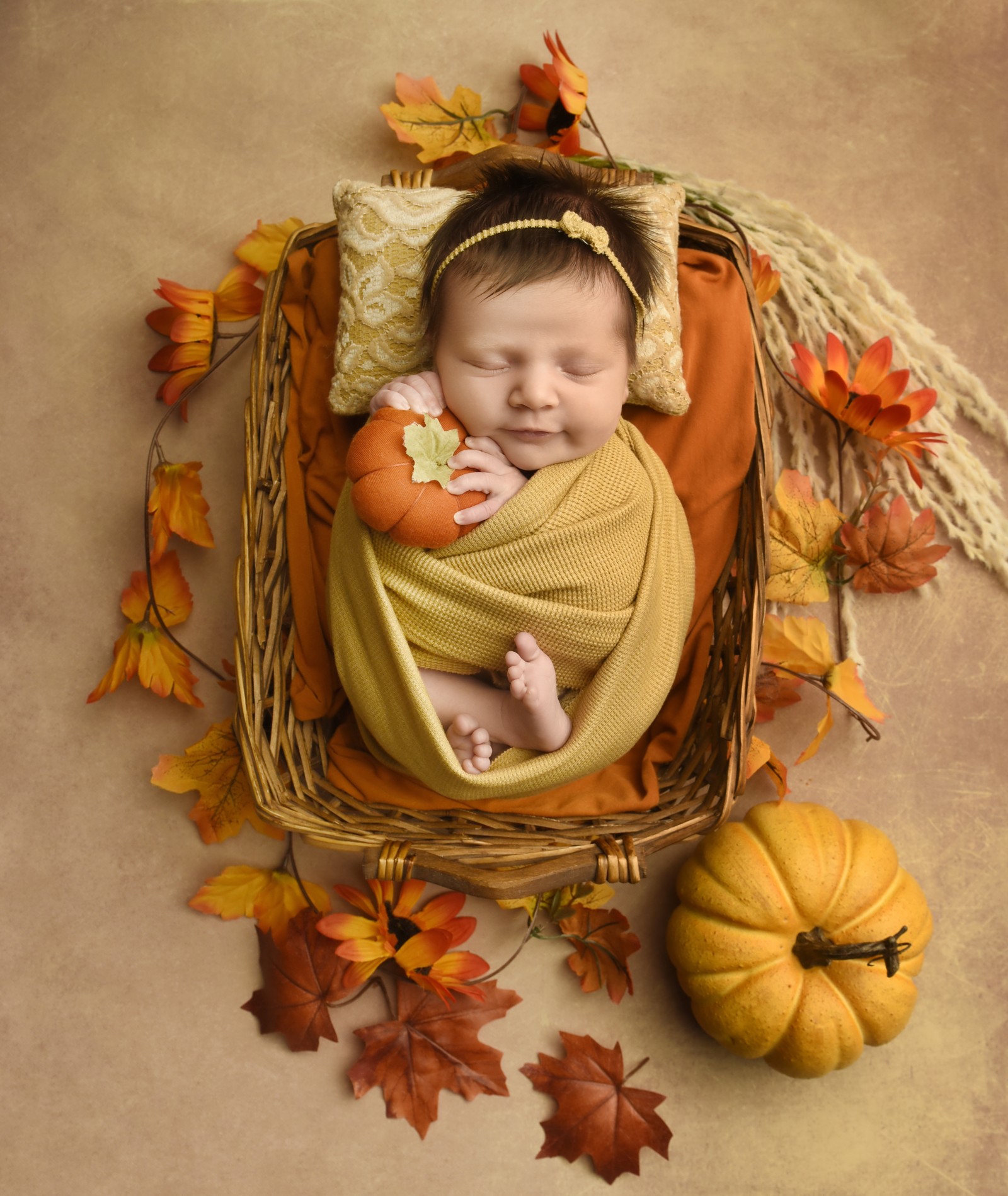 Sleeping newborn in a mustard wrap with autumn leaves and pumpkins